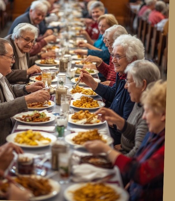 A long church-supper table full of seniors passing plates of fried chicken and sides